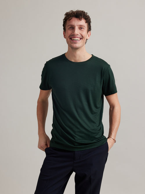 Man draagt een merinowollen T-shirt met korte mouwen in donkergroen met ronde hals in een gewicht van 170 g/m²